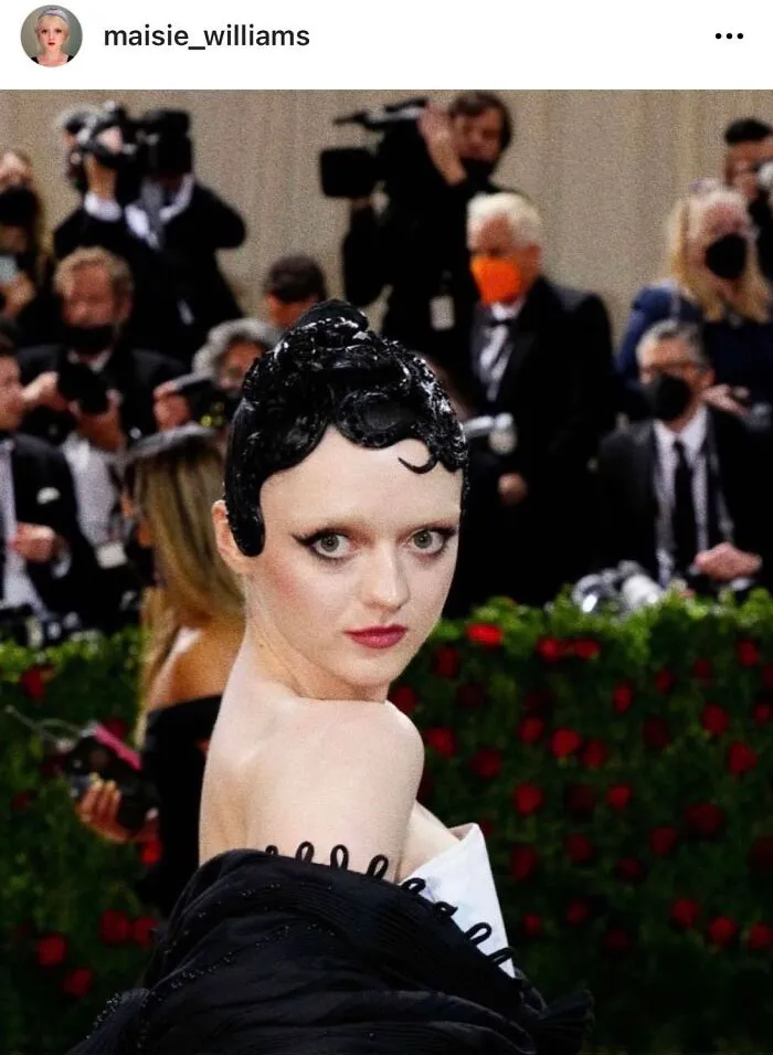 A person with a unique hairstyle at a formal event, capturing attention amid a crowd of photographers.