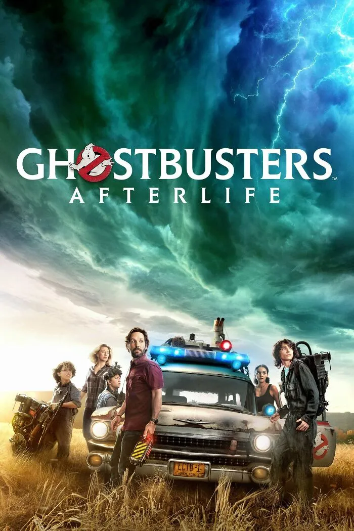 Cast of Ghostbusters Afterlife standing by the ghostbusting vehicle under stormy skies in horror comedy setting.