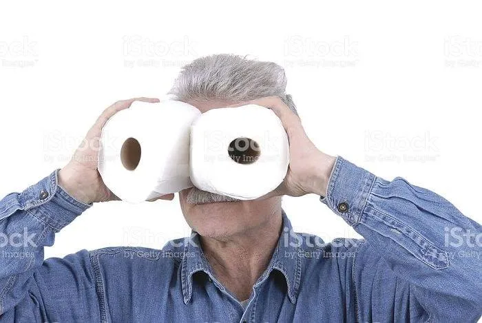 Man holding toilet paper rolls as binoculars in a weird stock image.