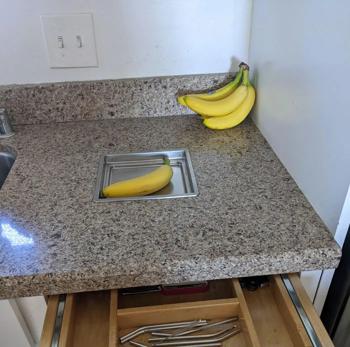 Alojados en un Airbnb y tenemos esta pequeña bandeja de metal incrustado en la encimera. Tiene unos 2,5 cm de profundidad (plátano como escala), no se puede quitar, y tiene un cajón debajo