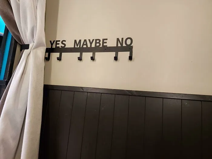 Wall-mounted black metal coat rack with hooks labeled yes, maybe, and no, showcasing a brilliant design idea.