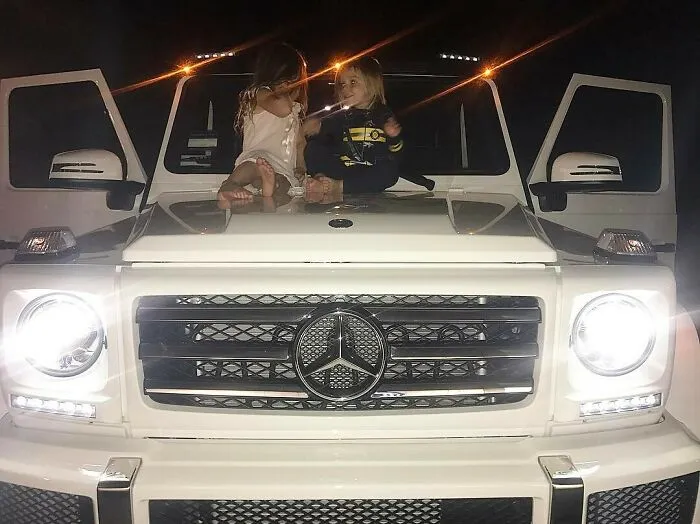 Children sitting on a luxury Mercedes SUV, highlighting celebrity wealth.