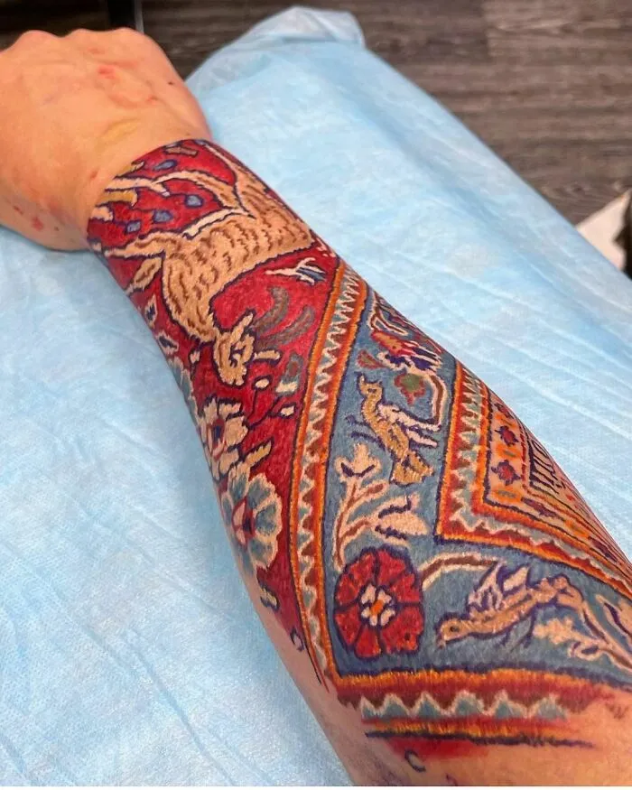 A forearm inked with a colorful, detailed tattoo resembling a Persian rug, showcasing creative tattoo art.