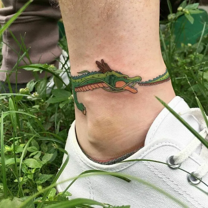 Unique ankle tattoo of a green dragon wrapping around the leg, captured outdoors with a white sneaker.