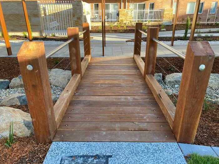 Un hermoso puente de madera dura que construimos en el trabajo. Accesible para sillas de ruedas. Viene con un bonito poste de acero casi en el centro. Esto es lo que pasa cuando los arquitectos se niegan a cambiar su plan incluso cuando el sentido común dice que hay que mover el puente