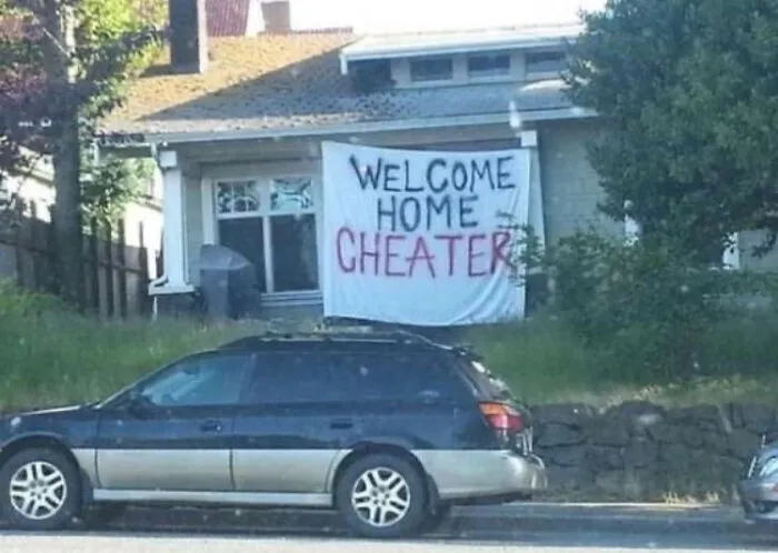 Funny sign on house reads "Welcome Home Cheater" with a car parked in front.