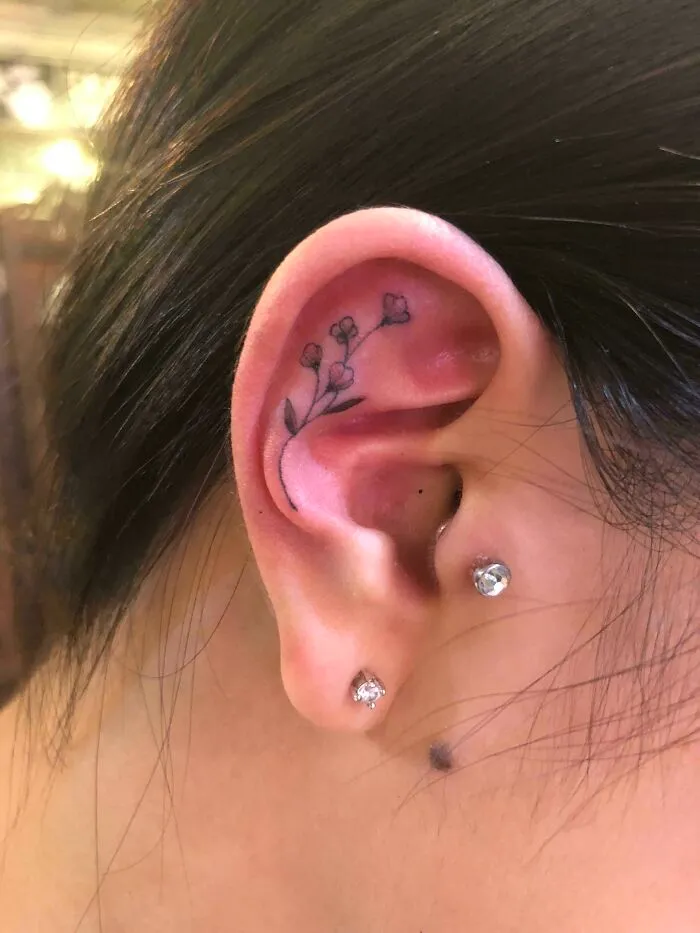 Delicate floral ear tattoo design with small buds and leaves behind the ear.
