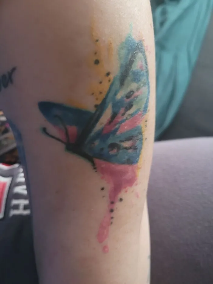 A colorful butterfly tattoo on an arm, featuring blue and pink watercolor effects.