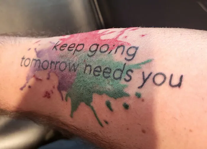 Colorful tattoo with motivational text: "keep going tomorrow needs you" on forearm.