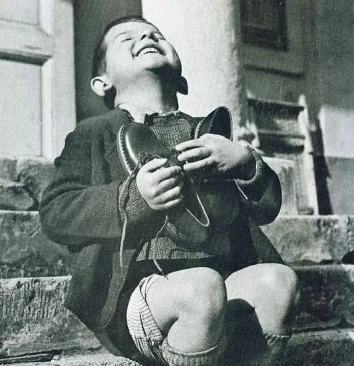 6-Year Old Austrian Boy, Beams With Unbounded Joy As He Clasps A New Pair Of Shoes Presented To Him By The American Red Cross, At The End Of World War 2, In 1945