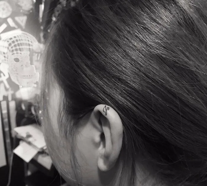 Minimalist ear tattoo with delicate script on the ear's edge, showcasing subtle artistry and unique style.