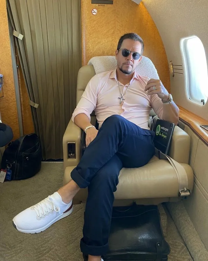 A celebrity in sunglasses and a pink shirt relaxes in a luxury private jet, showcasing wealth.