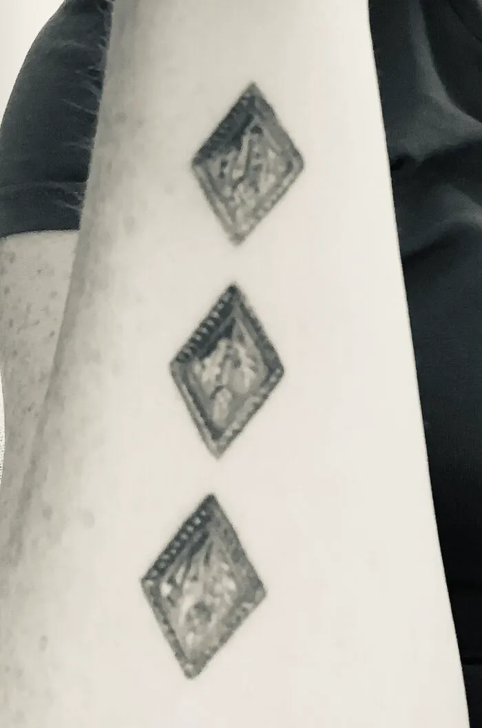 Three diamond-shaped tattoos in a vertical line on a person's forearm.