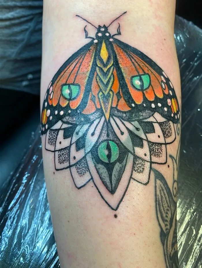 Colorful butterfly tattoo with geometric details and eye design on skin.