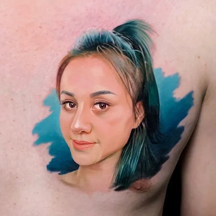 Hyper-realistic tattoo portrait of a woman with detailed facial features and blue background on skin.