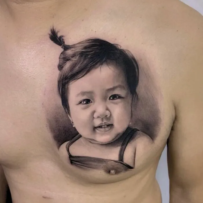 Hyper-realistic tattoo of a child's face on a person's chest, showcasing intricate details and lifelike features.