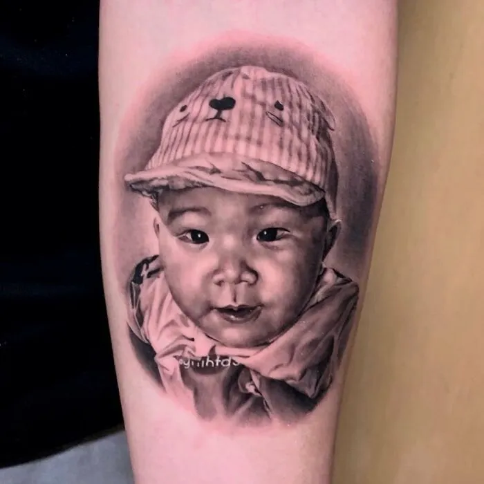 Hyper-realistic tattoo of a baby wearing a cap, seamlessly imprinted on the skin.