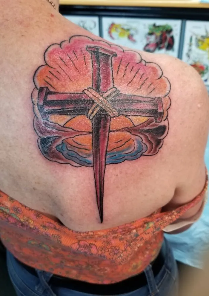 Colorful cross tattoo with clouds on a person's upper back, showcasing detailed artistry.