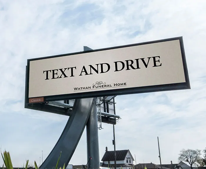 Funny sign on billboard reading "Text and Drive" by Wathan Funeral Home.