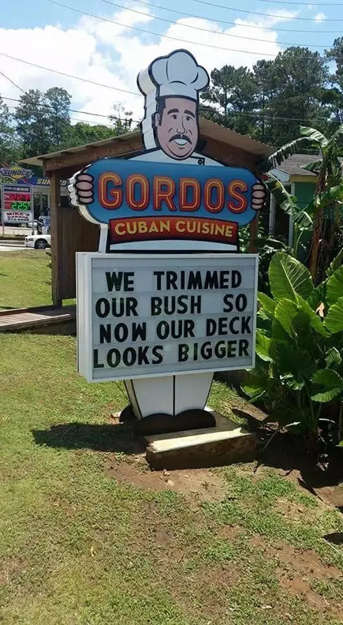 Funny sign outside Gordos Cuban Cuisine reading, "We trimmed our bush so now our deck looks bigger," with chef illustration.
