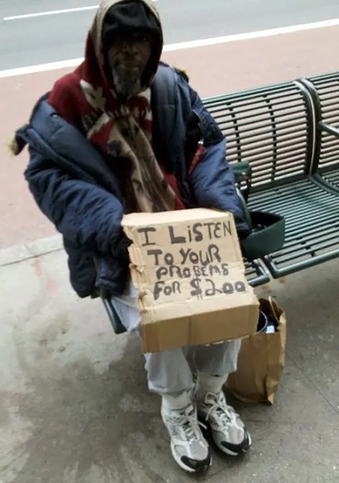 Man holding a sign offering to listen to your problems for $2, sitting on a bench with a paper bag beside him. Funny signs.