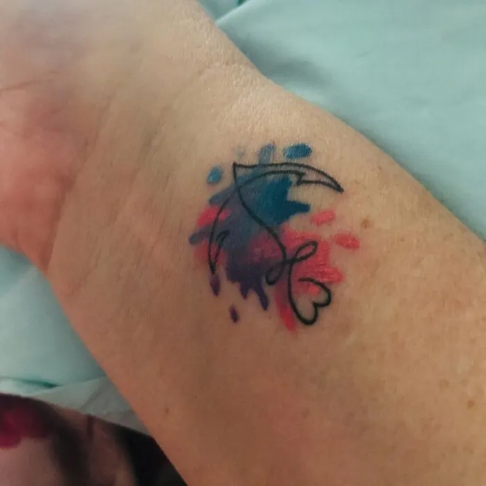 Colorful abstract tattoo on an arm featuring a black-line design with blue and pink watercolor splashes.