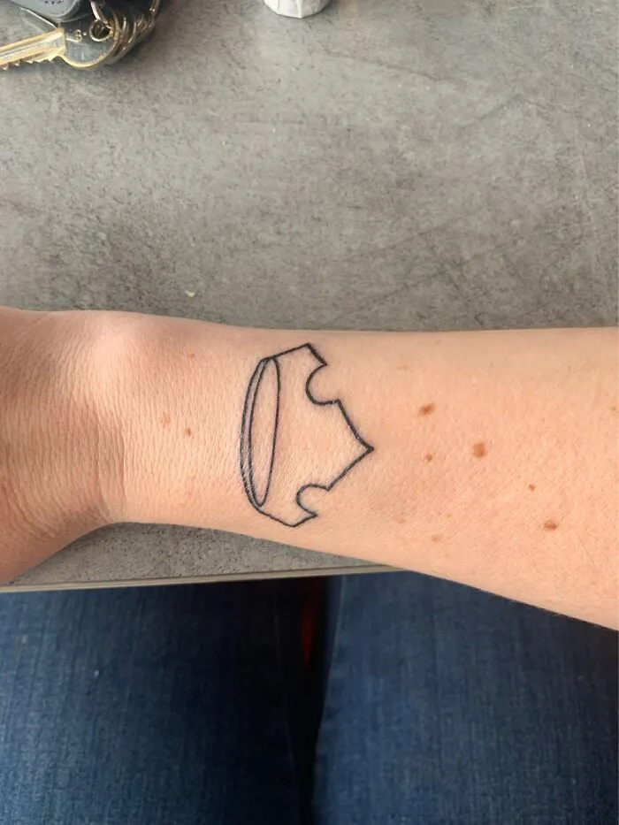 Tattoo of a razor blade on forearm, close-up view against a table surface.