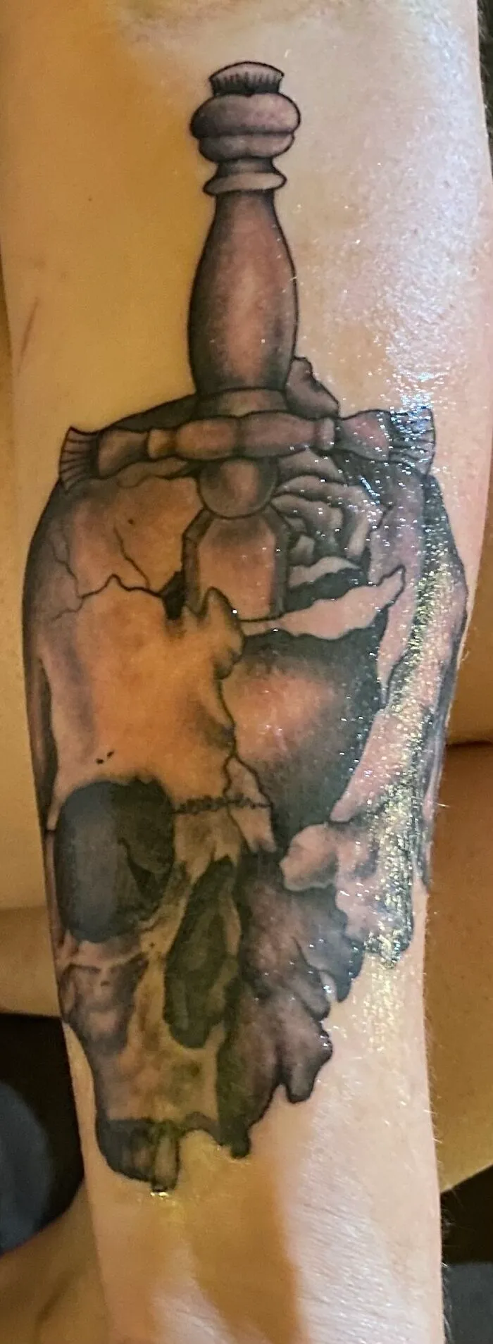 Tattoo of a cracked skull with a chess piece on top, showcasing unique art and design.