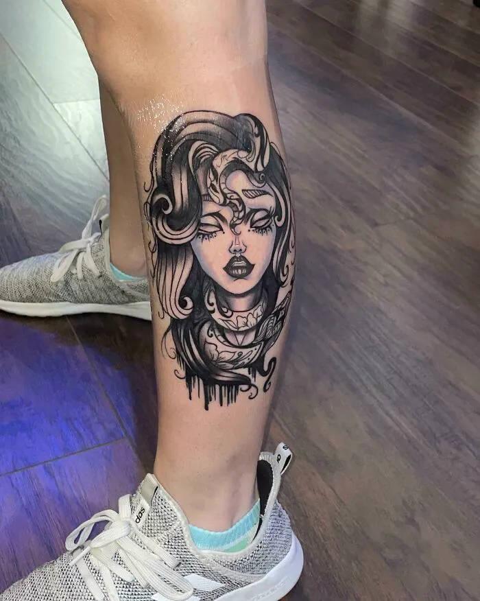 Lower leg tattoo featuring a woman's face with intricate black ink design.