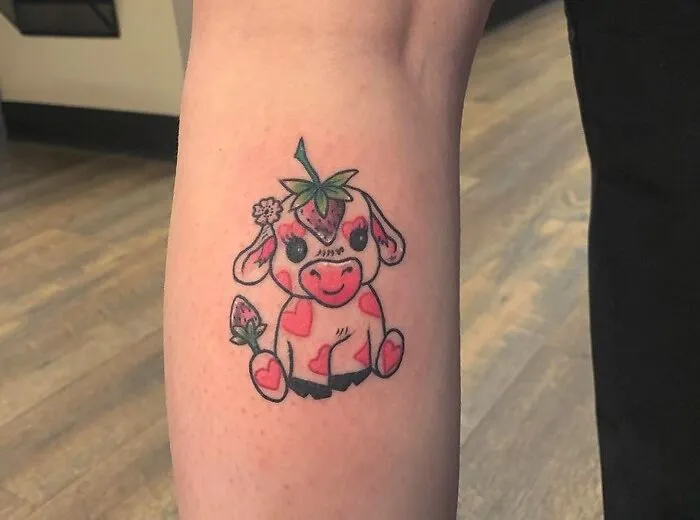 "Unique calf tattoo of a cute, colorful cow with strawberries and flowers on its body."