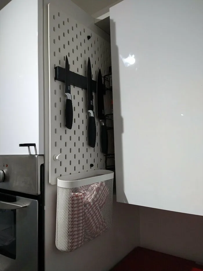 IKEA furniture hack: Knives stored on a magnetic strip and a mesh basket attached to a pegboard inside a cabinet.
