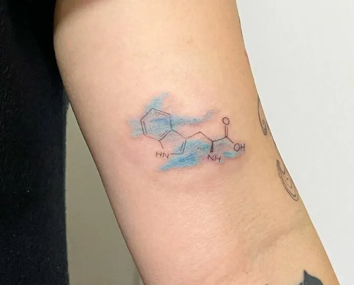Watercolor tattoo with a chemical structure on the arm, featuring blue shading.
