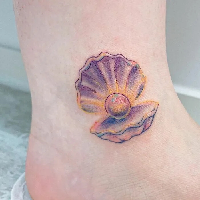 Watercolor tattoo of an open seashell with a pearl on an ankle.