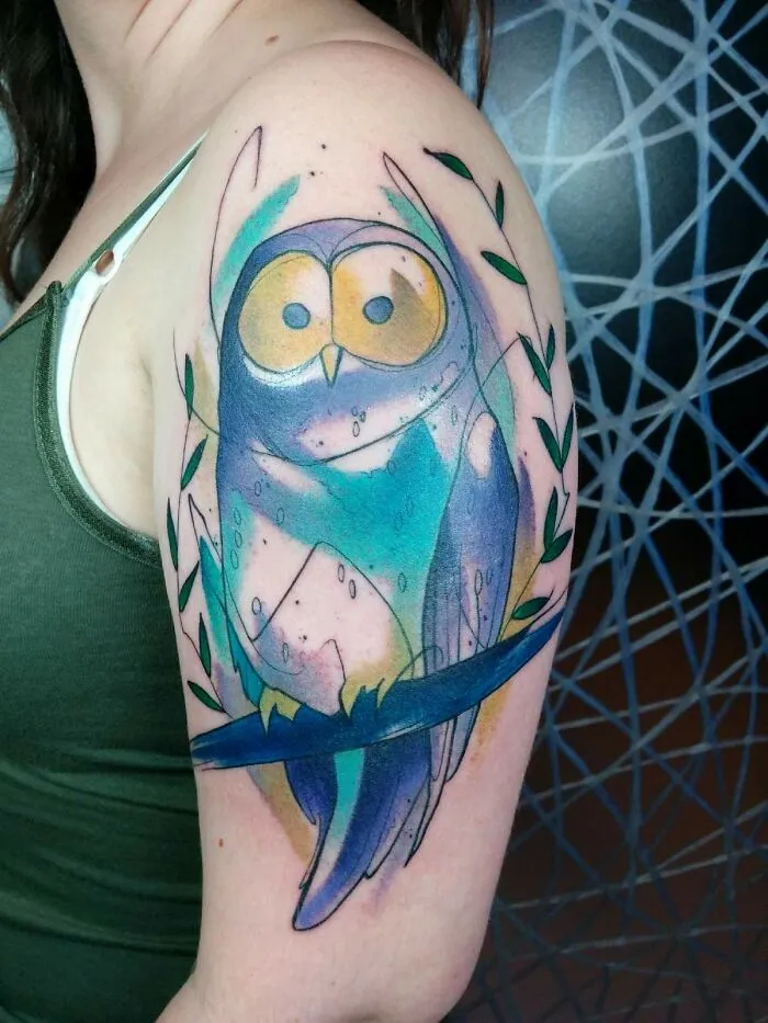 Watercolor tattoo of an abstract owl on an arm, featuring vibrant blues and greens for inkspiration.