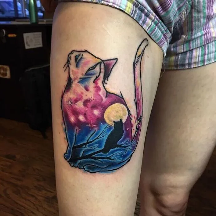 Watercolor tattoo of a cat with night sky and moon design on a person's thigh.