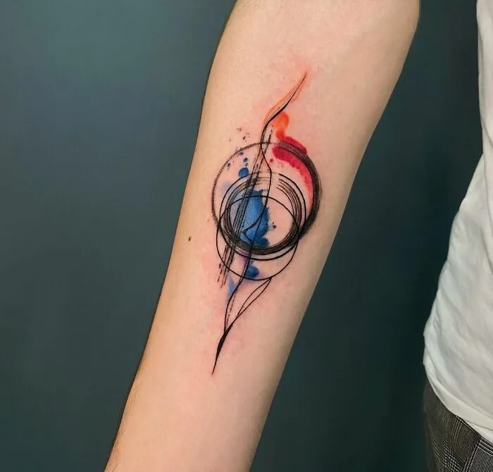 Abstract watercolor tattoo on forearm with colorful ink splashes and swirling black lines.
