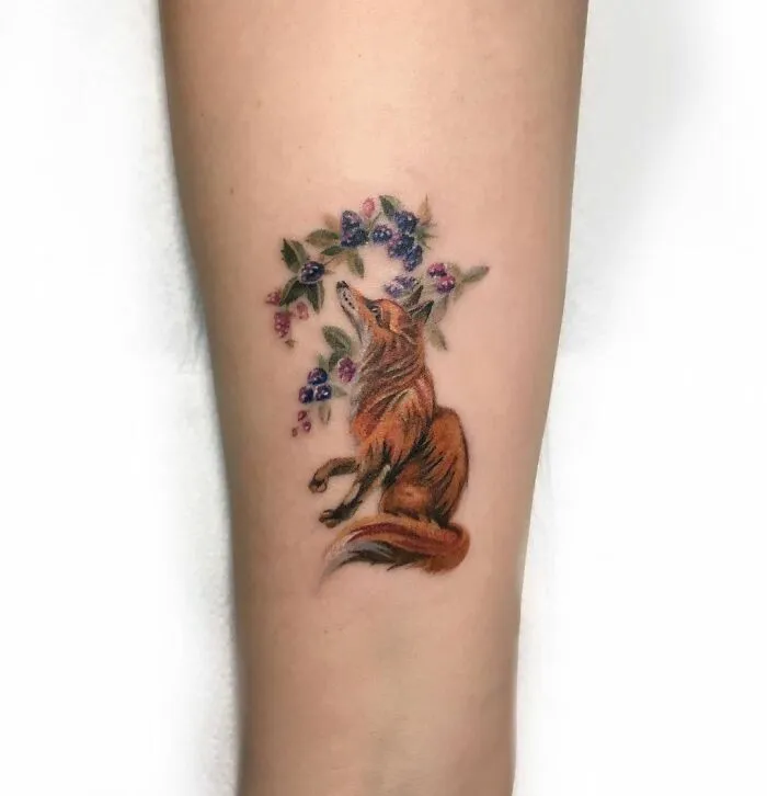 Watercolor tattoo of a fox surrounded by colorful flowers on forearm.