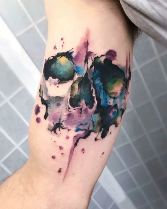 Watercolor tattoo on forearm with abstract splashes of color blending into a unique design.