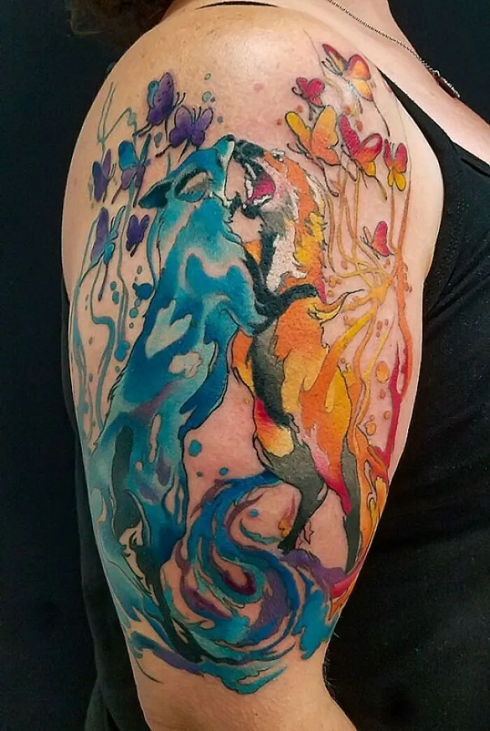 Vibrant watercolor tattoo of colorful foxes and butterflies on an arm.