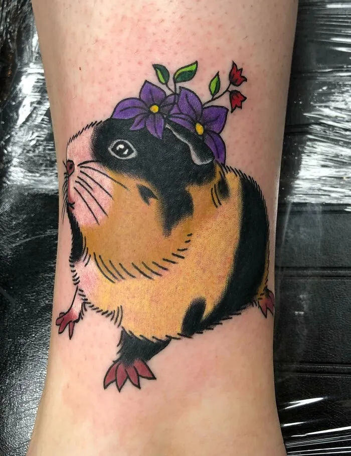 Guinea pig tattoo with purple flowers on its head, symbolizing the bond between humans and pets.