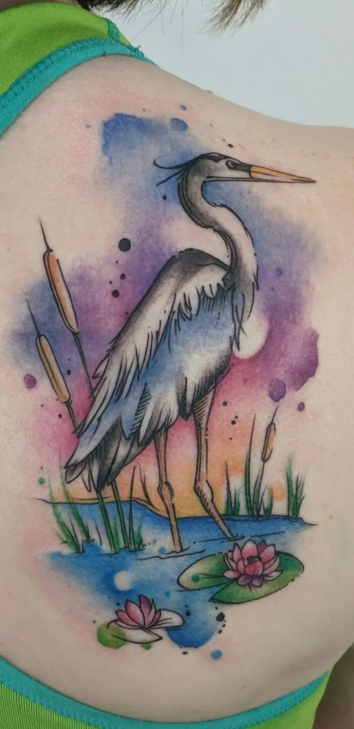 Watercolor tattoo of a heron standing in a pond with vibrant florals on the back.