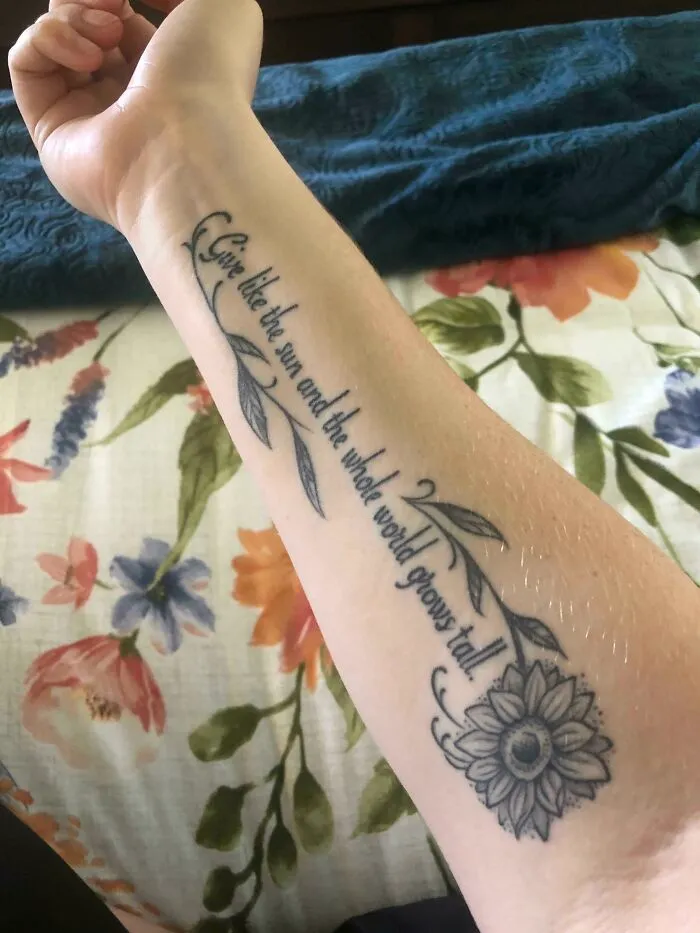 Close-up of a creative word tattoo on an arm, featuring a floral design and inspirational quote.
