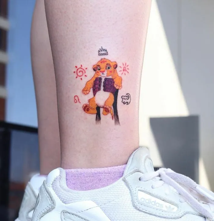 Tattoo of Rafiki holding Simba, offering a sweet hit of cartoon nostalgia on a person's leg above an Adidas shoe.