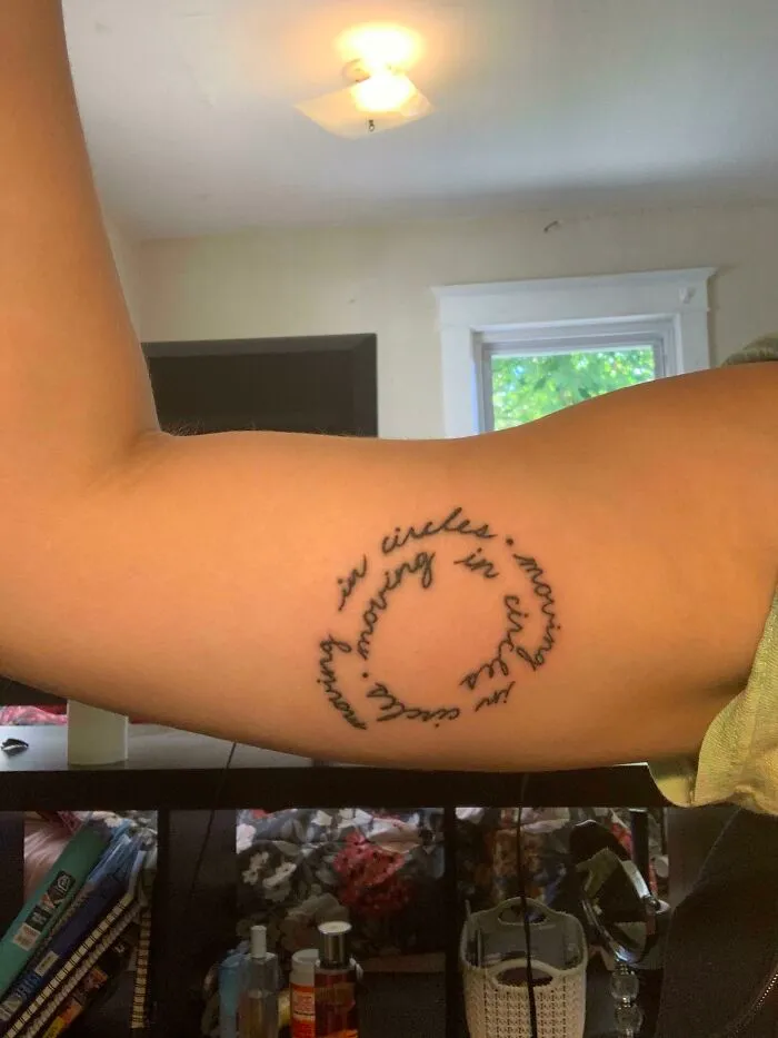 Circular script word tattoo on inner arm in bright room setting.