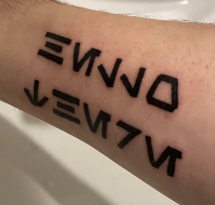 Arm with creative word tattoo in bold, black geometric script for inkspiration.