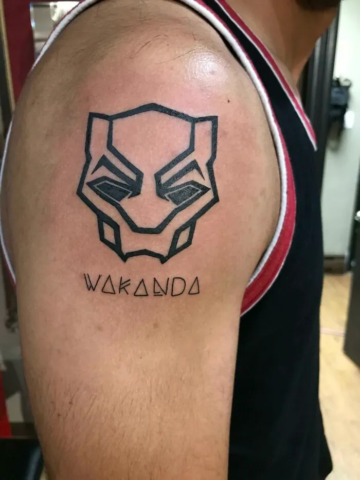 Marvel tattoo of Black Panther mask and "Wakanda" text on upper arm.
