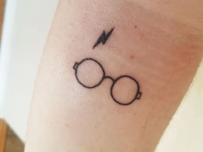 Minimalist tattoo of round glasses and a lightning bolt, symbolizing a fictional character.