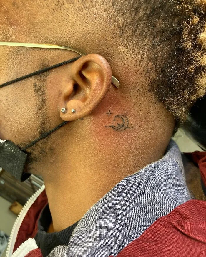 Minimal moon and star ear tattoo with earrings visible.