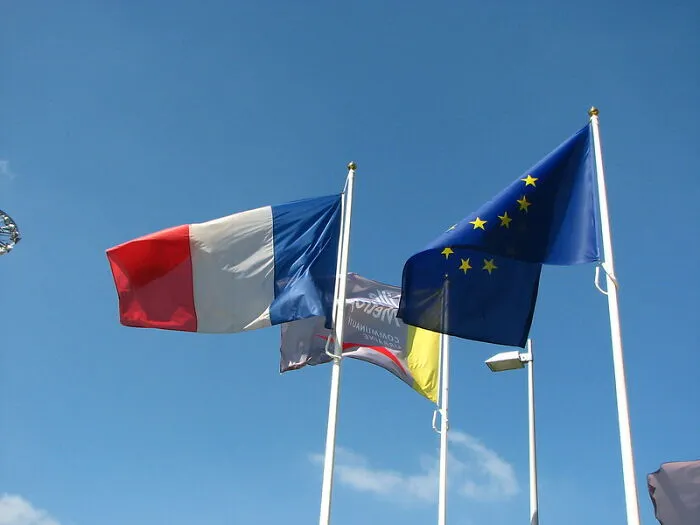 Flags, including French and EU flags, waving against a clear blue sky.