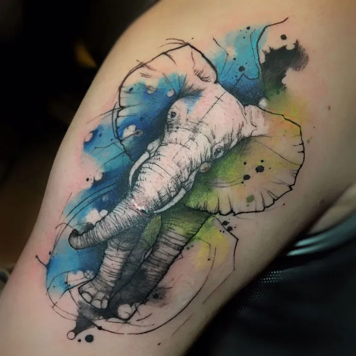 Watercolor tattoo of an elephant with vibrant blue and green splashes on arm, showcasing inkspiration artistry.